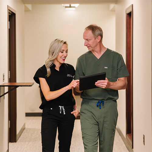 Two surgeons walking down a hallway while they review a folder.
